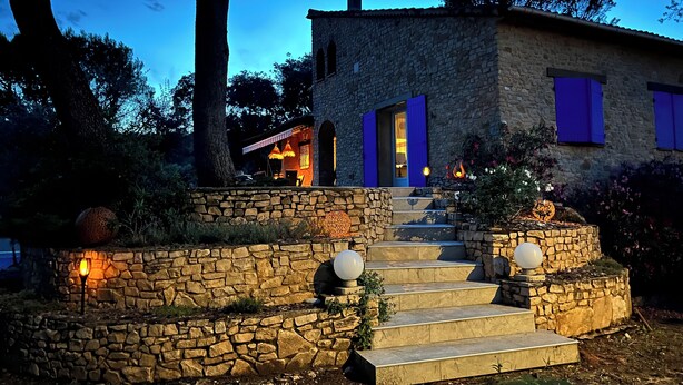 Une maison en pierre avec un escalier en pierre menant à l’entrée, entourée d’arbres et d’un jardin.