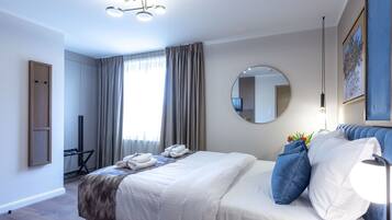 A modern hotel room with a neatly made bed, a round mirror, a desk with a chair, and a large window with curtains.