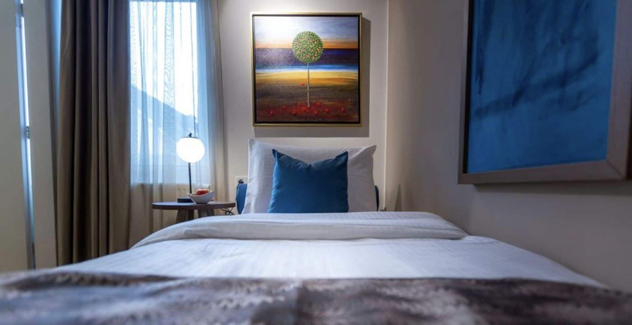 A hotel room with a bed, a nightstand, a lamp, and a painting on the wall.