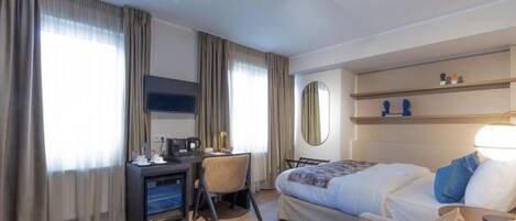 A hotel room with a bed, desk, chair, and a TV.