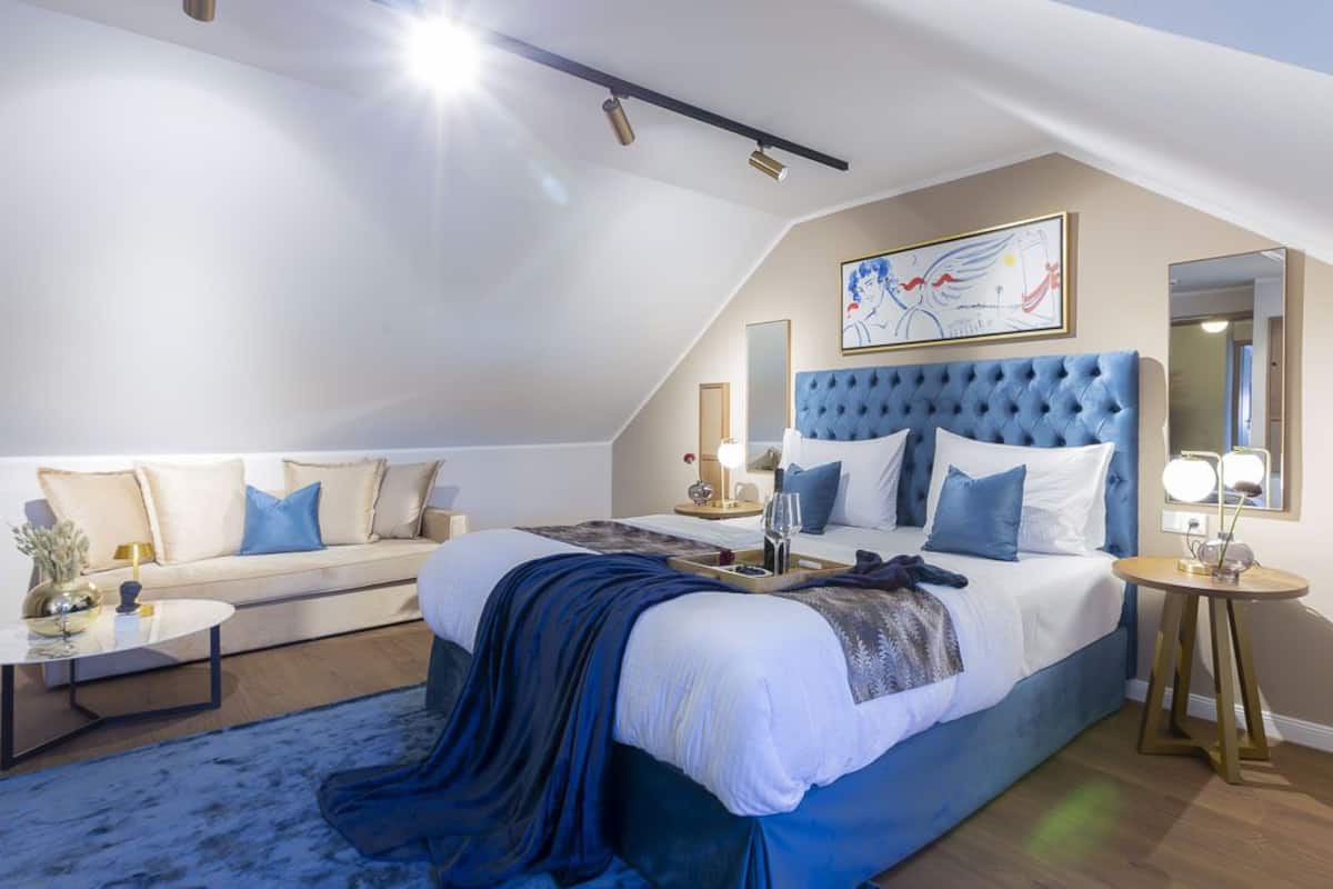 A modern bedroom with a large bed, a sofa, a round coffee table, and a bedside table with lamps.