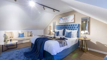 A modern bedroom with a large bed, a sofa, a round coffee table, and a bedside table with lamps.