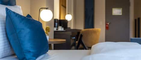 Habitación de hotel con cama, almohadas azules, escritorio con lámpara y una silla.