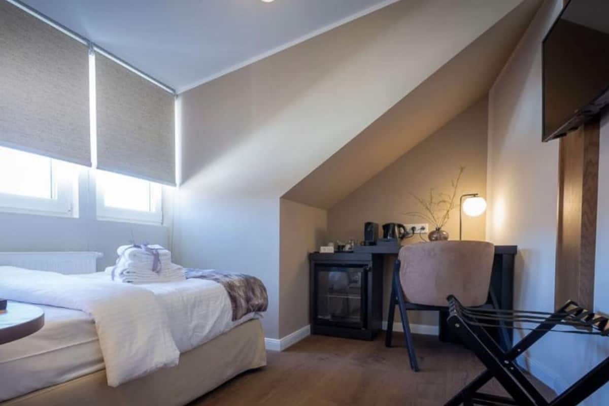A bedroom with a bed, a desk, a chair, and a small table with items on it.