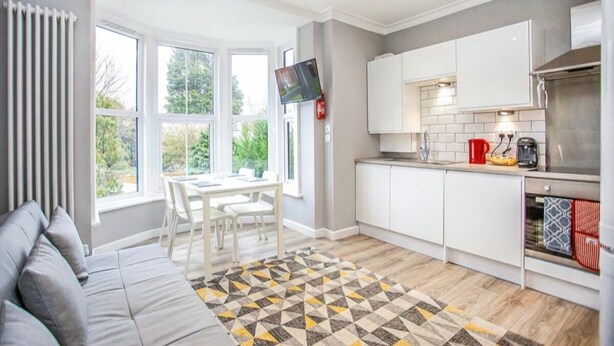 A modern kitchen with white cabinets, a built-in oven, and a window overlooking greenery. - Watford WD18 - Homely 2Bedroom/1Bathroom Flat w/ FREE WIFI & FREE PARKING (Watford)