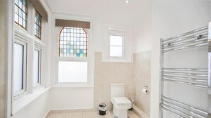 A bathroom with a bathtub, toilet, and a window with stained glass. - Watford WD18 - Homely 2Bedroom/1Bathroom Flat w/ FREE WIFI & FREE PARKING (Watford)