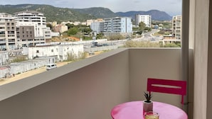 Un balcón con mesa y sillas, con vistas a un paisaje urbano con edificios y una calle.
