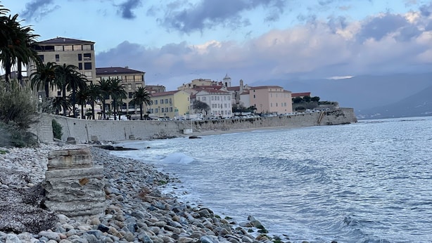 Un pueblo costero con una playa rocosa, edificios a lo largo de la orilla y vista al mar.