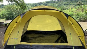 A yellow tent with a black base, set up in a natural environment with trees and a river in the background. - Camping Ground Taman Nggirli (Srimulyo)