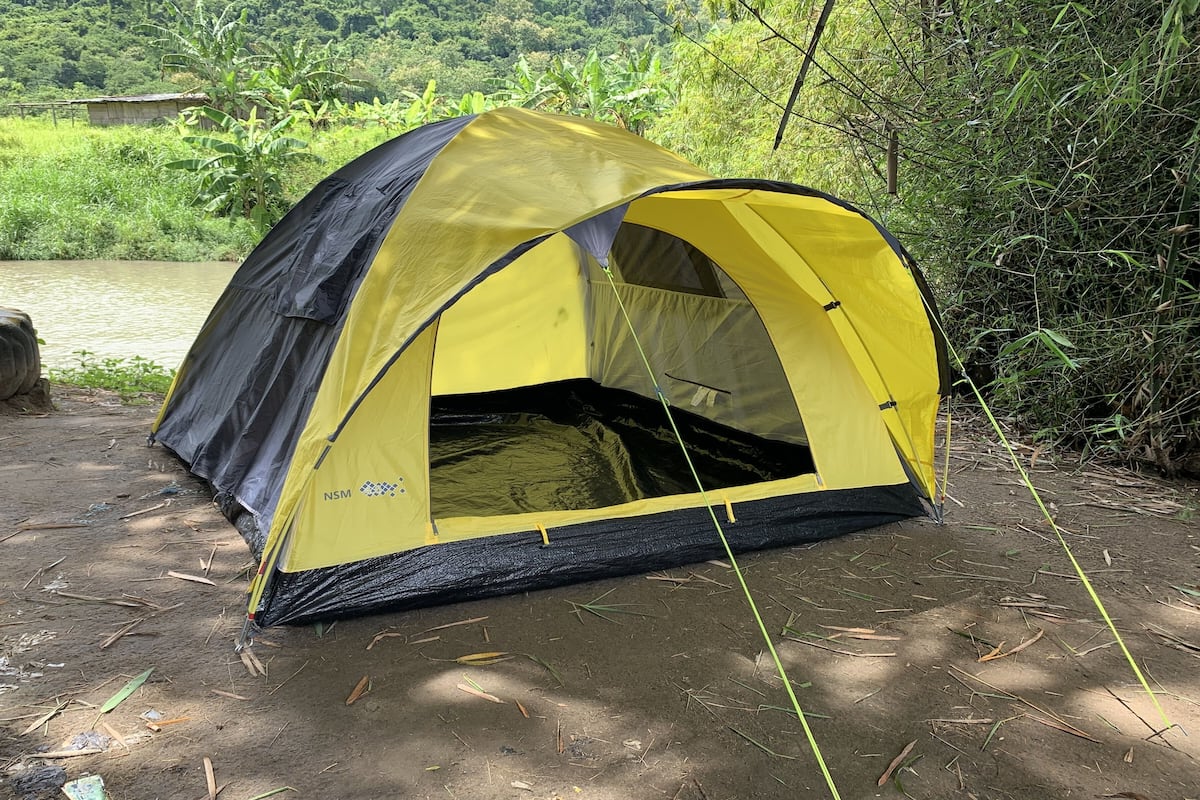 A yellow and black tent set up near a river, surrounded by greenery.