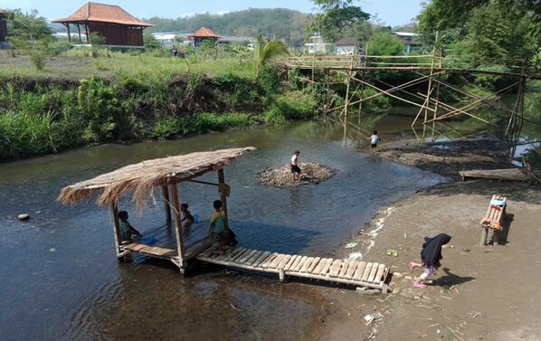 Orilla de río con una construcción de techo de paja, un puente de madera y un pequeño muelle.