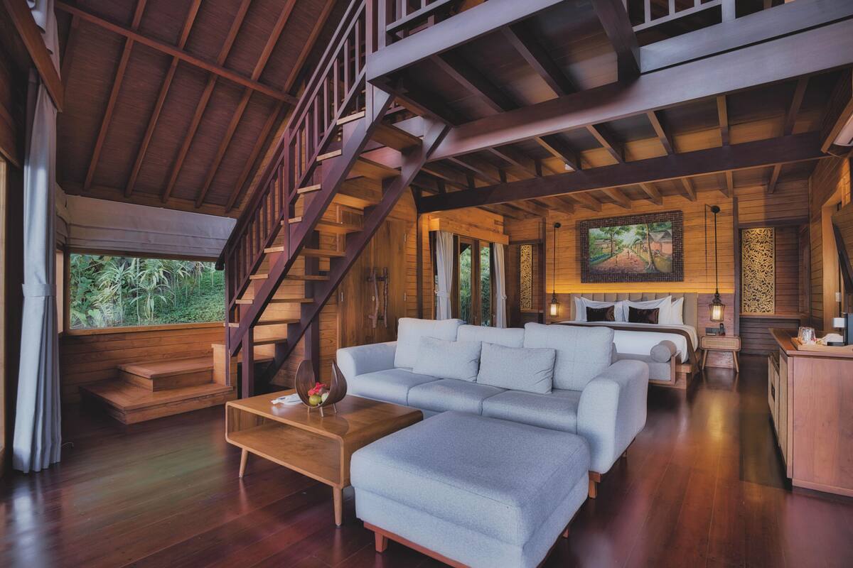 Una habitación amplia con un sofá grande, una mesa de centro de madera y una escalera que sube a un nivel superior.