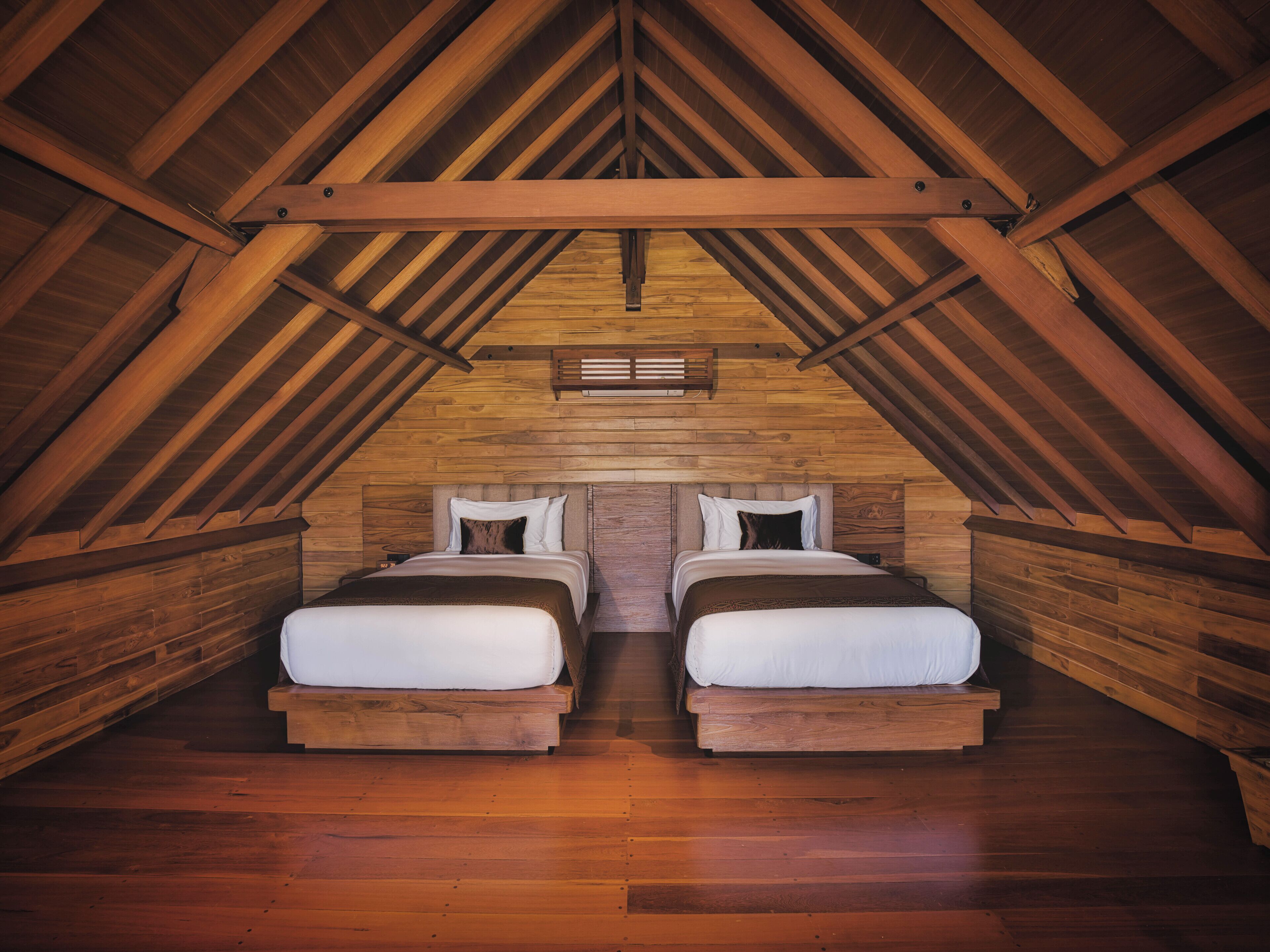 A cozy attic bedroom with two beds, wooden beams, and a sloped ceiling.