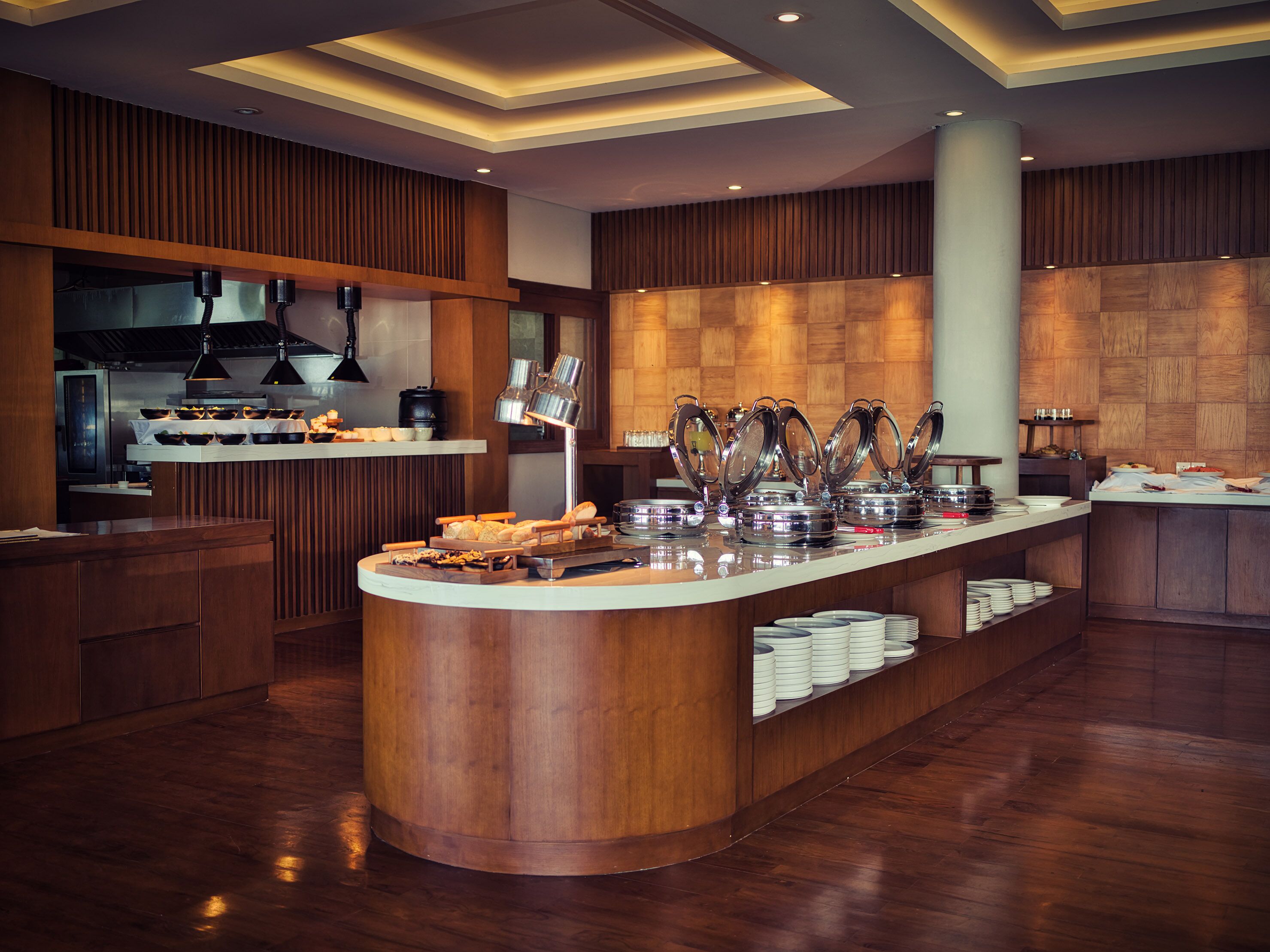 Een moderne keuken met een centraal eiland, houten lambrisering en een buffet met diverse gerechten en bestek.