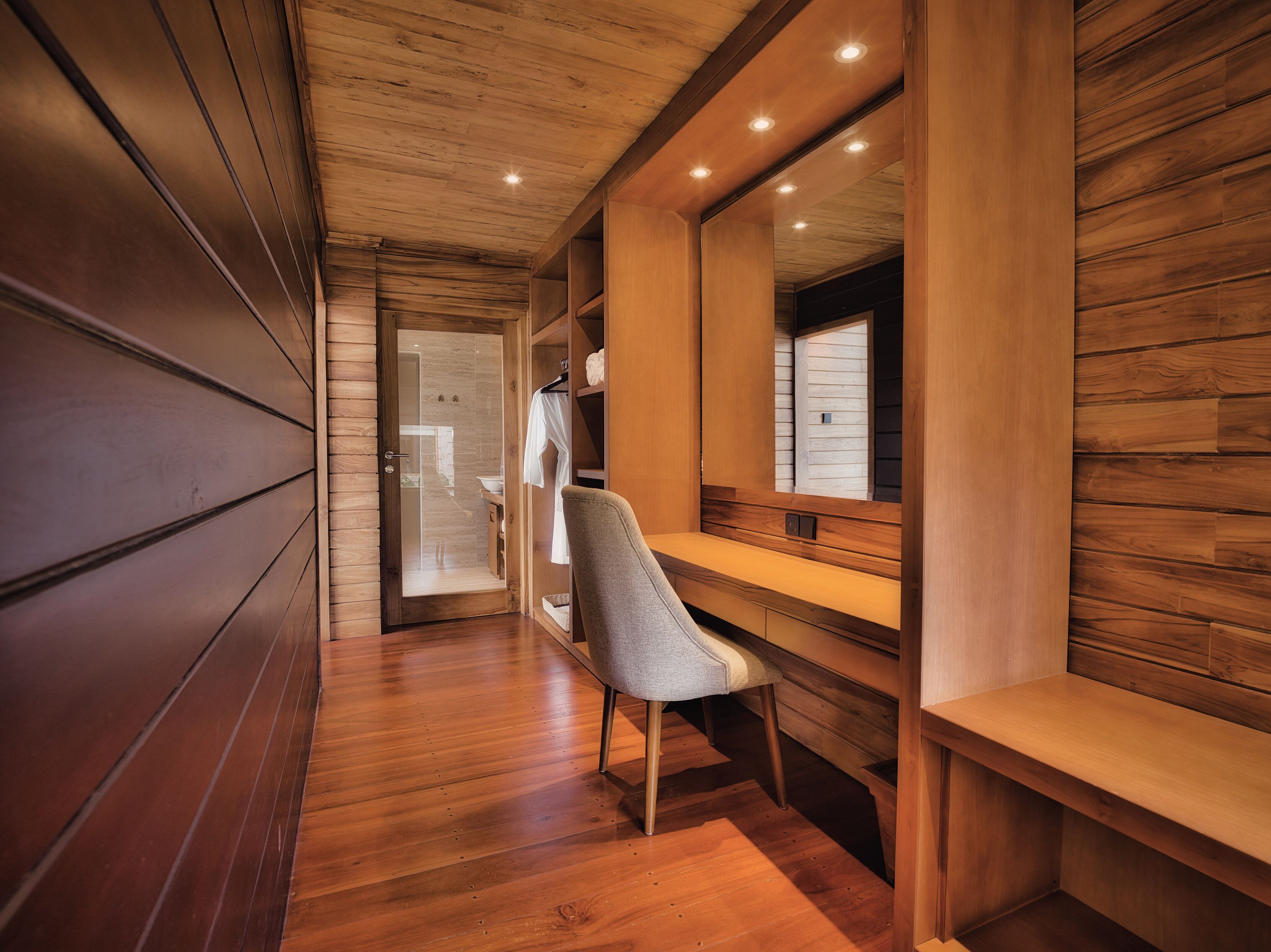 A hallway with wooden flooring, a bench, and a chair.