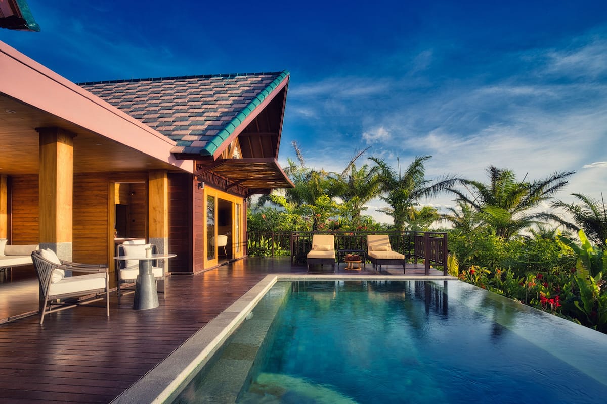 Un resort moderno con piscina, terraza de madera y plantas tropicales.