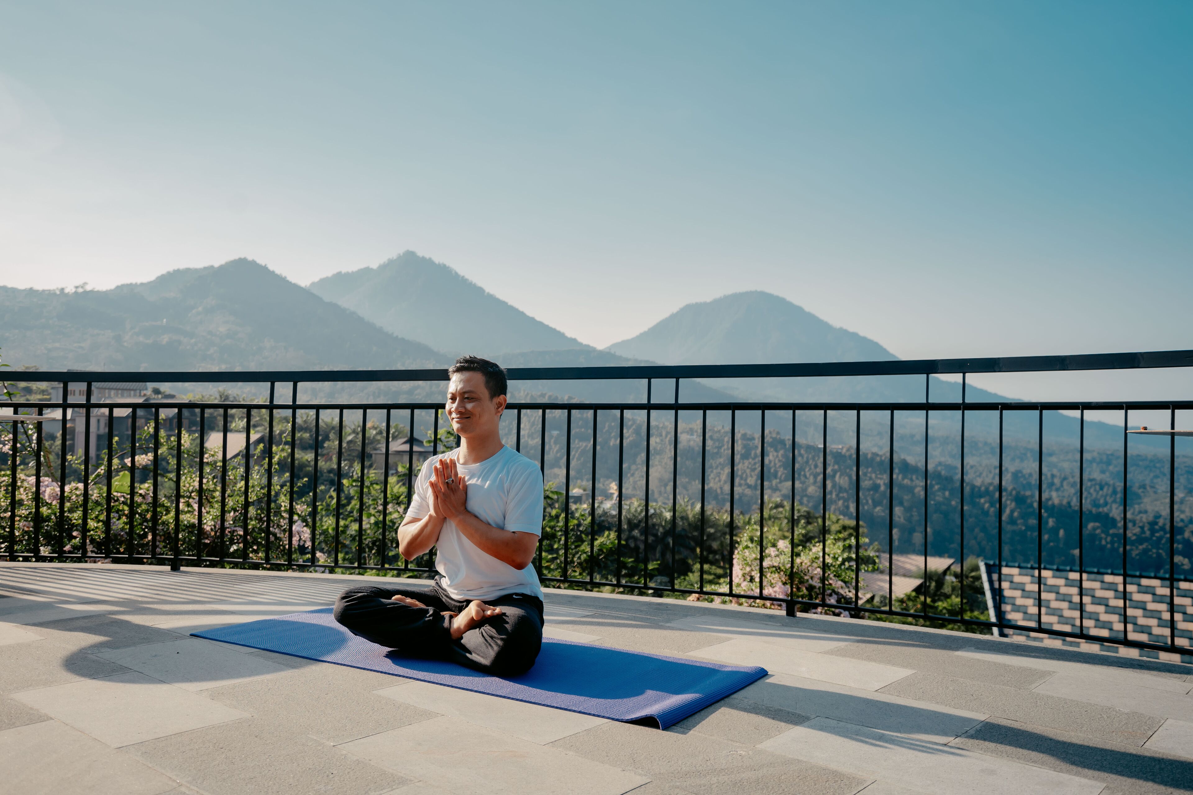 A person meditating on a blue mat with a mountainous landscape in the background.