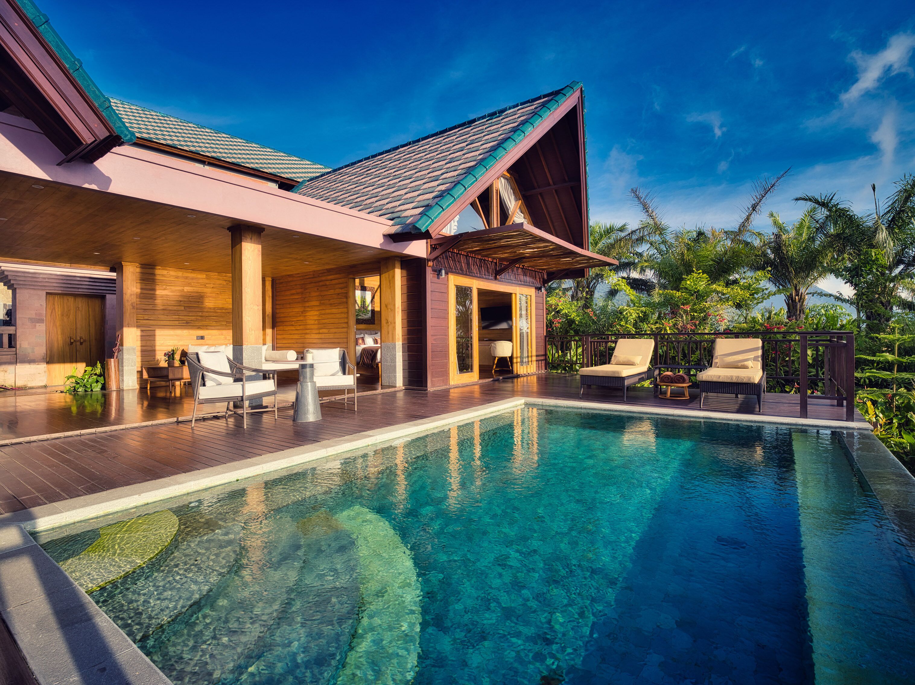 A resort with a swimming pool, outdoor seating, and a covered area with wooden flooring.