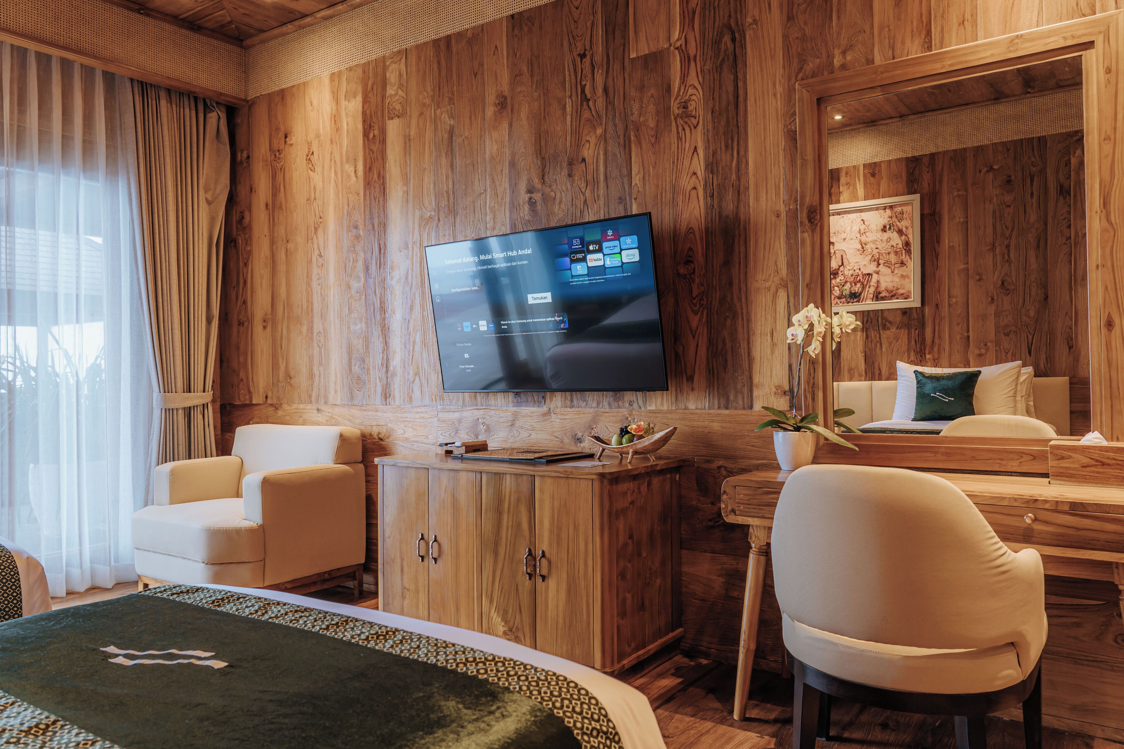 Habitación de hotel con pared de madera, un televisor de pantalla plana sobre un escritorio de madera, una cama con manta verde y una planta en maceta.