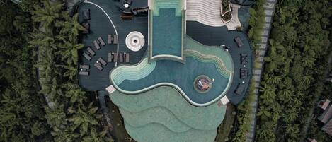 An aerial view of a resort with a central pool shaped like a guitar, surrounded by lounge areas and dense greenery.
