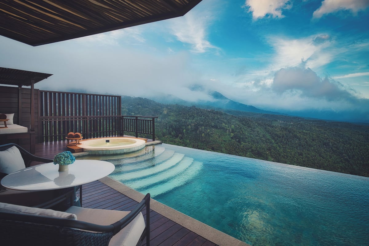 Una piscina infinita con cubierta de madera, mobiliario exterior y un jacuzzi.