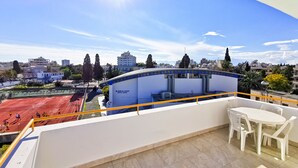 Terraço no telhado com vista para um centro esportivo, quadra de tênis e edifícios ao redor.