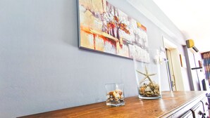 Um balcão de madeira com objetos decorativos, uma grande pintura abstrata na parede e uma porta ao fundo.