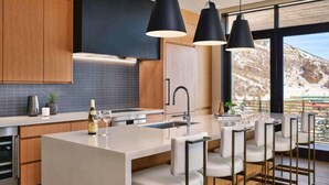 A modern kitchen with a central island, bar stools, pendant lighting, and a view of a snowy mountain. - One Snowmass East 307 (Snowmass)