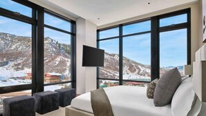 A bedroom with a large bed, a flat-screen TV, and a view of a snowy mountain landscape. - One Snowmass East 307 (Snowmass)