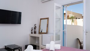 A hotel room with a bed, a TV, a desk, a mirror, and a view of the outside. - Villa Kocis with Private Pool (Santorini)