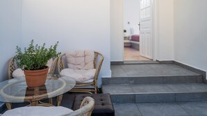 A small outdoor seating area with wicker chairs and a glass table, a potted plant, and a view of a white door leading to a room. - Villa Kocis with Private Pool (Santorini)