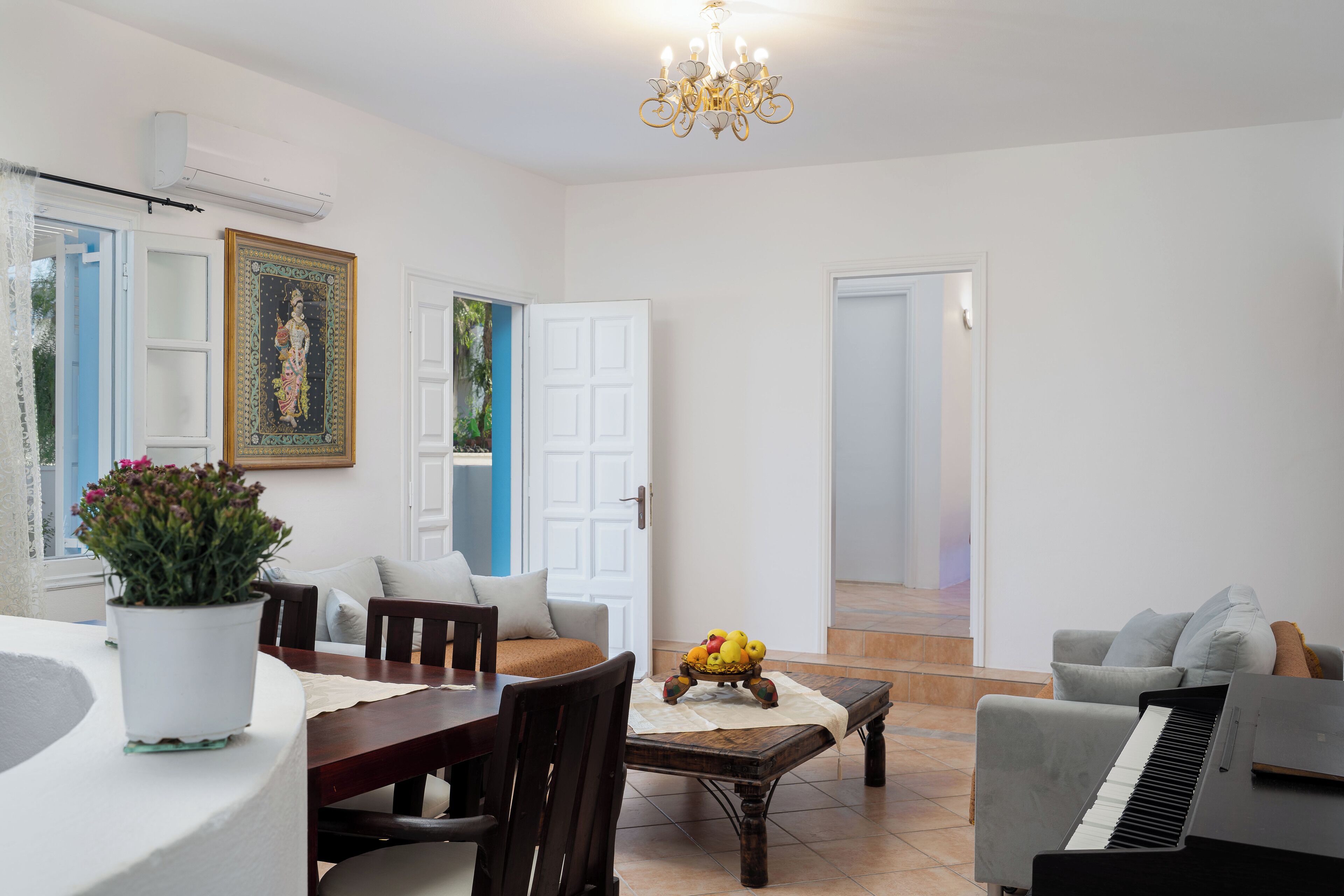 A spacious living room with a piano, a dining table with chairs, a potted plant, and a framed artwork on the wall.