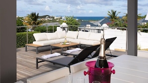 A balcony with a white sofa, a wooden coffee table, and a table with a bottle of champagne. - Villa Z’Abricot – Spacious Family Villa with Recreational Amenities Near Orient Bay, St. Martin (Cul-de-Sac)