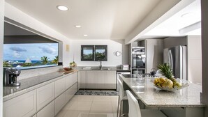 A modern kitchen with a view of the ocean, a coffee machine, and a fruit bowl on the counter. - Villa Z’Abricot – Spacious Family Villa with Recreational Amenities Near Orient Bay, St. Martin (Cul-de-Sac)