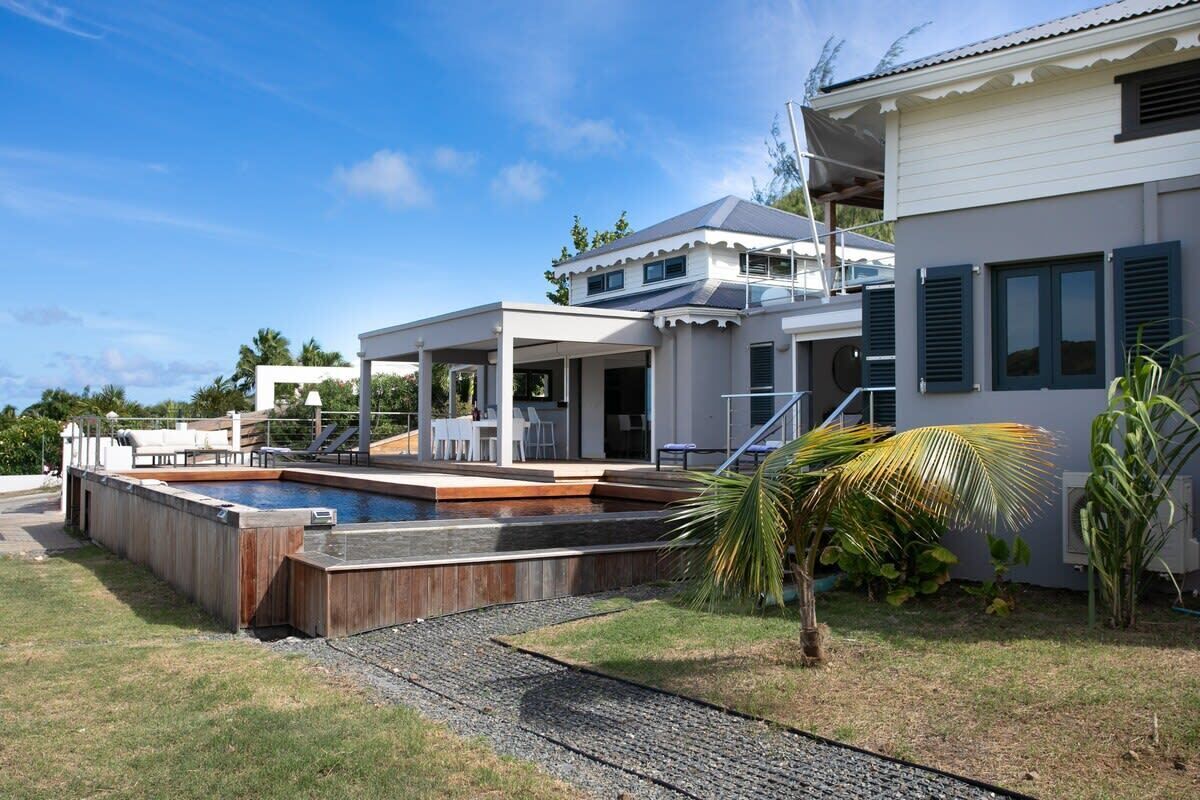 Una casa moderna con piscina, un patio cubierto y un césped bien cuidado.