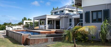 Una casa moderna con piscina, un patio cubierto y un césped bien cuidado.