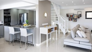 A modern kitchen with a central island, bar stools, and a staircase leading to a loft bedroom. - Villa Z’Abricot – Spacious Family Villa with Recreational Amenities Near Orient Bay, St. Martin (Cul-de-Sac)