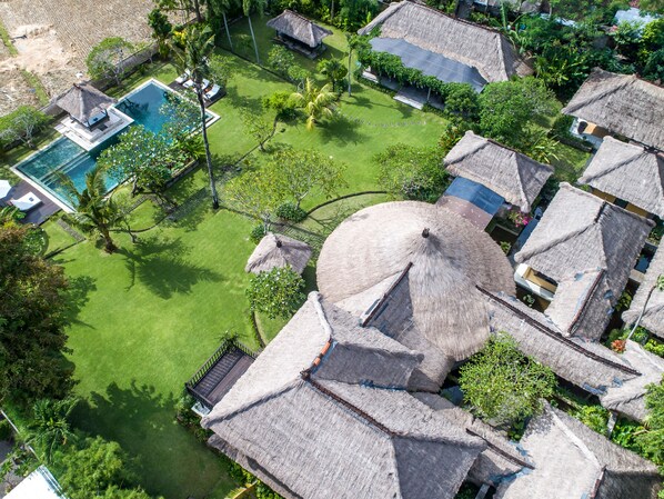 An aerial view of a resort with thatched-roof cottages, a swimming pool, and lush greenery. - Istana Semer (Kerobokan)