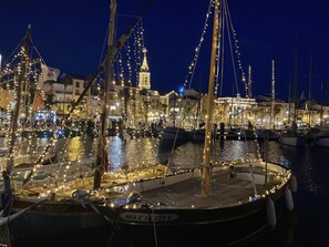 A marina at night with boats decorated with lights, a prominent tower, and buildings in the background. - LUXURY 2-ROOM APARTMENT - 50 M² - 2-STAR RATING - SANARY NEAR THE BEACHES & TOWN (Sanary-sur-Mer)