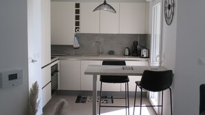 A modern kitchen with white cabinets, a central island, a hanging light fixture, and a window providing natural light.