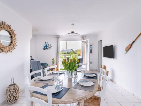 A dining area with a round table set for four, white chairs, a vase with flowers, and a view of the outdoors through a glass door.