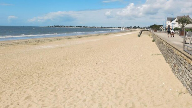 A sandy beach with a stone wall and a few people walking along the promenade. - La Perle de Damgan by Interhome (Damgan)