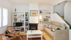 Una sala de estar con chimenea, sofás blancos, sillas de mimbre, una mesa de centro y una estantería.