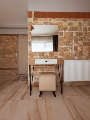 Features a stone wall, wooden vanity with a mirror, and a comfortable stool.