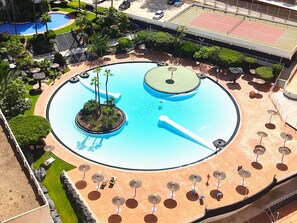 Una piscina circular con dos islotes, rodeada de palmeras y tumbonas.