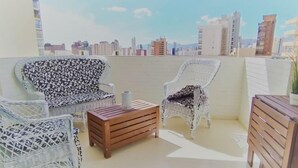 Un balcón con mobiliario de mimbre, una mesa de madera y vistas a un paisaje urbano.
