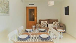 Un comedor con una mesa dispuesta para cuatro personas, un sofá e iluminación en el techo.