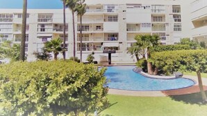 Un hotel de varios pisos con piscina rodeada de vegetación y palmeras.