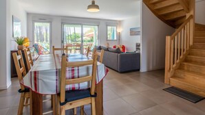 A spacious living area with a dining table set for four, a sofa, and a wooden staircase. - Les Fougères by Interhome (Moliets)