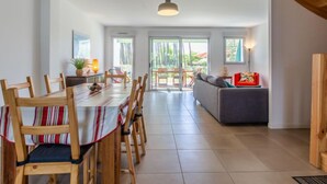 A spacious dining area with a long table and chairs, a sofa, and a view of the outdoors through large windows. - Les Fougères by Interhome (Moliets)